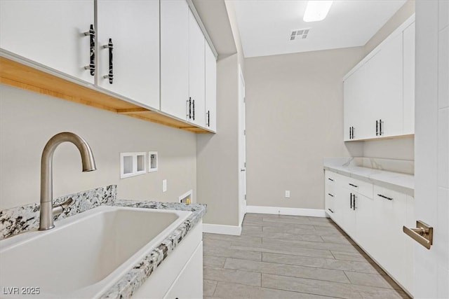 kitchen with baseboards, visible vents, white cabinets, and a sink