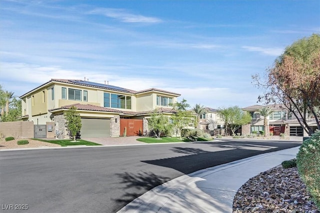 view of front of house with driveway, a tiled roof, fence, roof mounted solar panels, and stucco siding