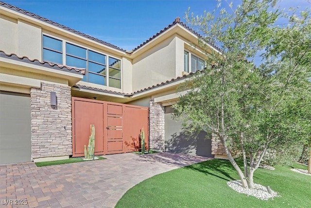 view of front of property with a tile roof, stucco siding, a front yard, a garage, and stone siding