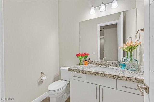 half bathroom featuring vanity, toilet, and baseboards