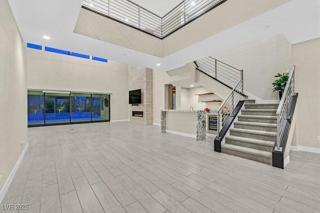 unfurnished living room featuring stairs, a fireplace, a high ceiling, and wood finished floors