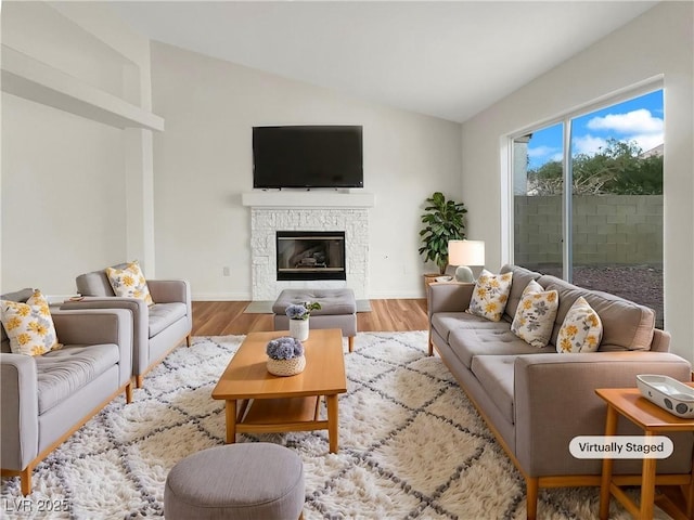 living room with a stone fireplace, vaulted ceiling, and light wood-type flooring