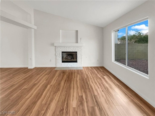 unfurnished living room featuring vaulted ceiling, a fireplace, baseboards, and light wood finished floors