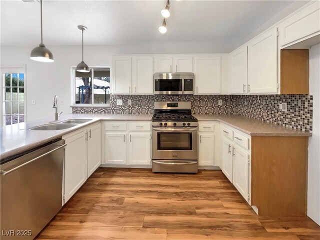 kitchen with backsplash, stainless steel appliances, light wood-style floors, white cabinetry, and a sink