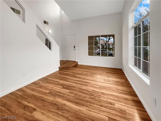 interior space featuring visible vents, baseboards, wood finished floors, and a towering ceiling