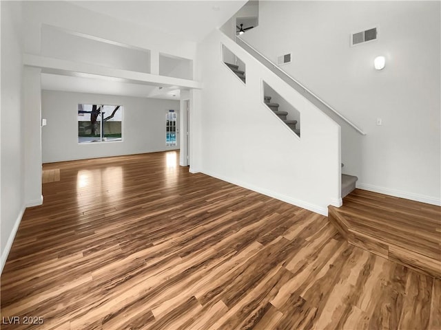 unfurnished living room featuring stairs, wood finished floors, visible vents, and baseboards