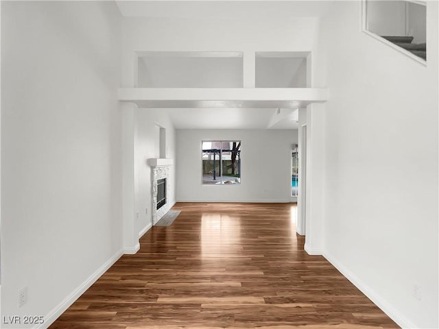 unfurnished living room featuring a glass covered fireplace, wood finished floors, and baseboards