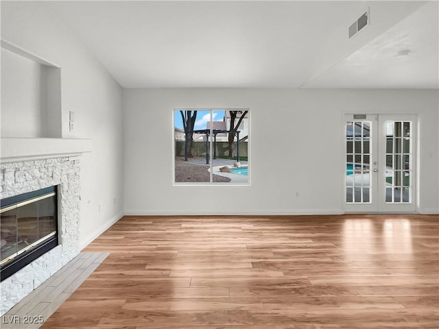 unfurnished living room featuring wood finished floors, visible vents, baseboards, a stone fireplace, and french doors