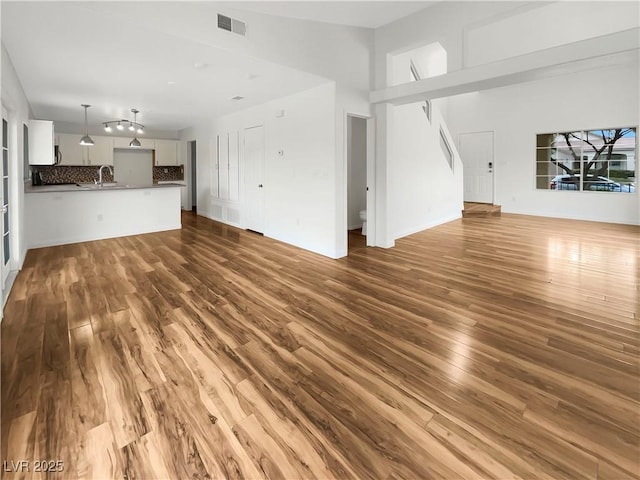 unfurnished living room with wood finished floors, visible vents, a towering ceiling, and a sink