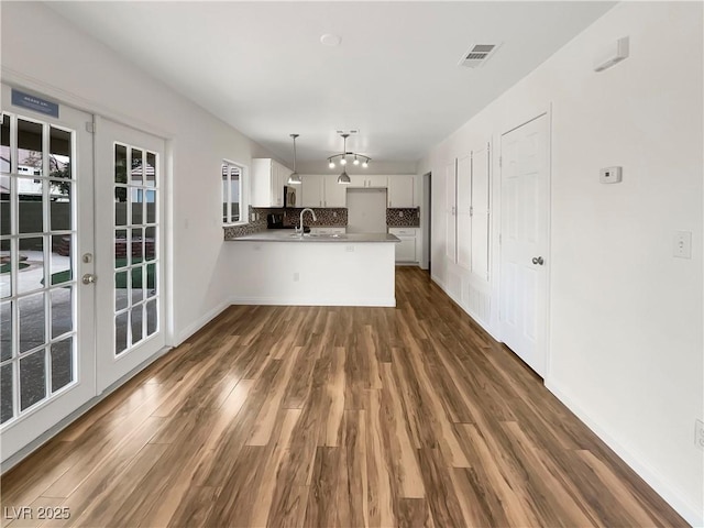 kitchen with tasteful backsplash, pendant lighting, a peninsula, white cabinets, and dark wood-style flooring