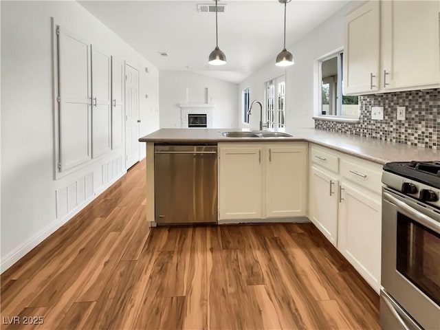 kitchen with visible vents, decorative backsplash, a peninsula, stainless steel appliances, and a sink