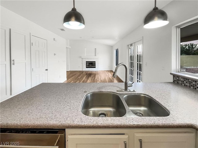 kitchen featuring a sink, decorative light fixtures, open floor plan, a glass covered fireplace, and dishwasher