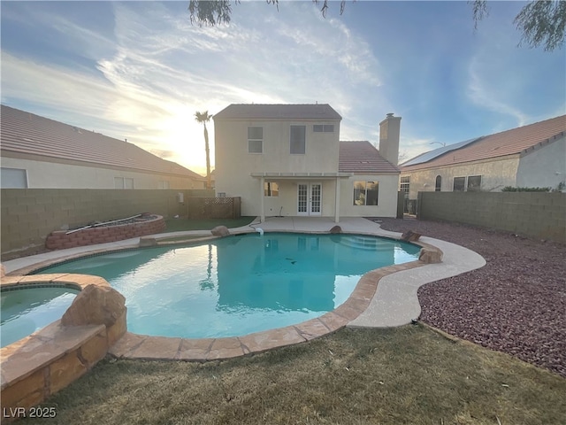 pool at dusk featuring a fenced backyard, french doors, and an in ground hot tub