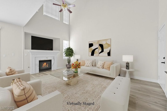 living room featuring ceiling fan, a towering ceiling, a fireplace, and light hardwood / wood-style floors