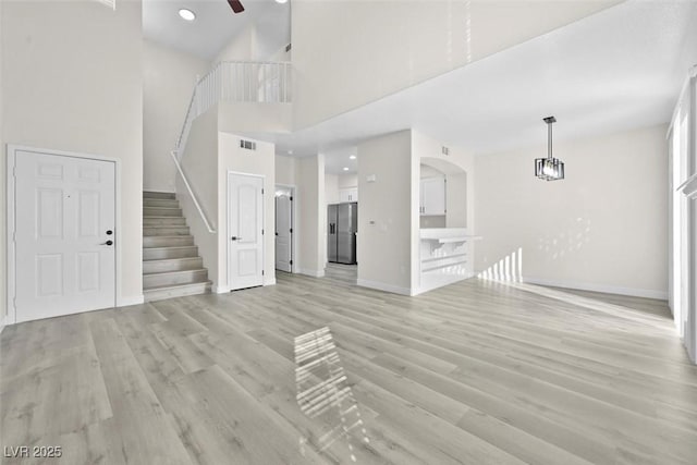 unfurnished living room with light hardwood / wood-style floors, ceiling fan, and a high ceiling