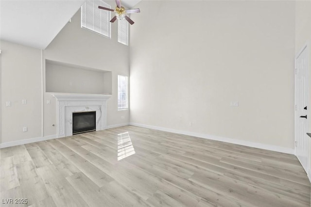 unfurnished living room featuring ceiling fan, a towering ceiling, a fireplace, and light hardwood / wood-style floors