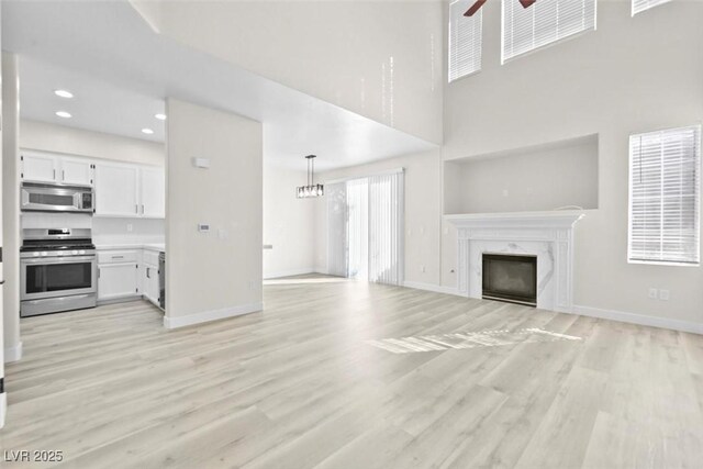 unfurnished living room with a premium fireplace, a towering ceiling, ceiling fan with notable chandelier, and light wood-type flooring