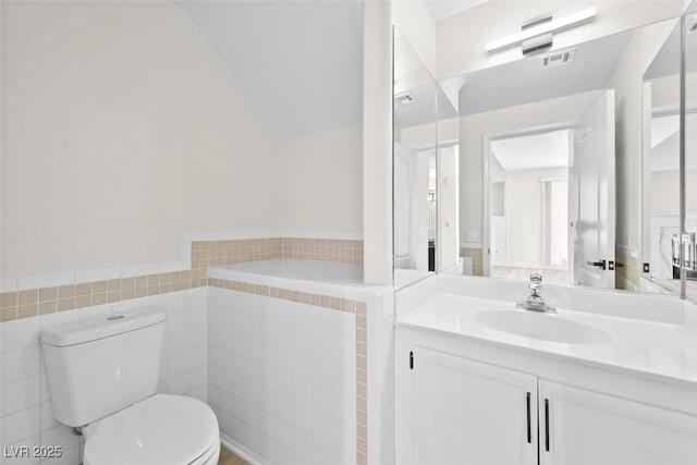 bathroom with vanity, vaulted ceiling, tile walls, and toilet