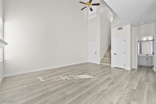 unfurnished living room with light hardwood / wood-style floors, ceiling fan, and a high ceiling