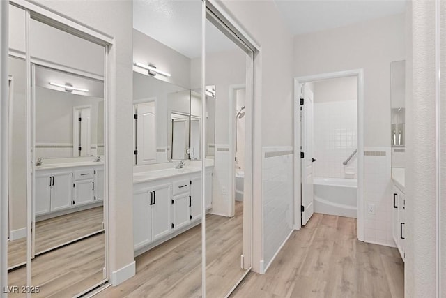 bathroom with wood-type flooring, a tub, tile walls, and vanity