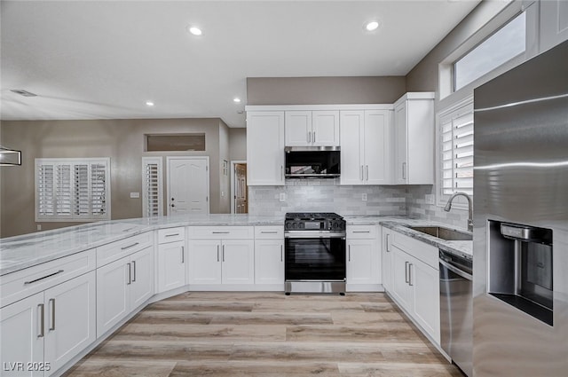 kitchen featuring stainless steel appliances, white cabinetry, light stone countertops, and sink