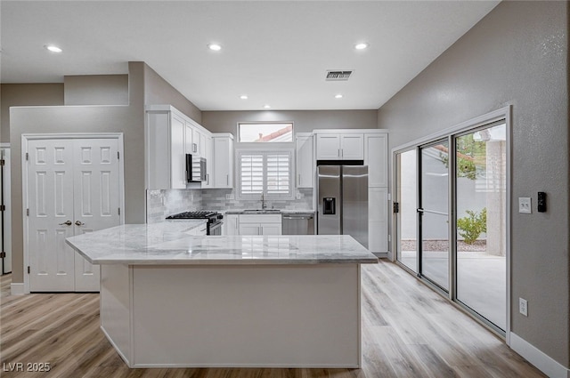 kitchen featuring sink, appliances with stainless steel finishes, white cabinetry, light stone countertops, and decorative backsplash