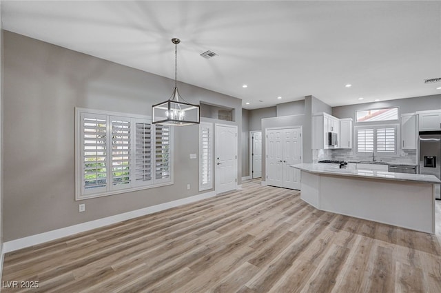 kitchen featuring appliances with stainless steel finishes, white cabinets, light hardwood / wood-style floors, and decorative backsplash