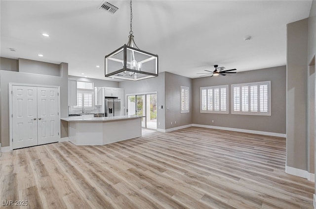 kitchen with stainless steel refrigerator with ice dispenser, white cabinetry, light hardwood / wood-style flooring, and decorative light fixtures