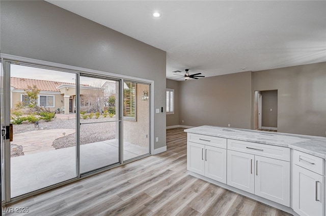 kitchen with white cabinetry, light stone countertops, light wood-type flooring, and ceiling fan