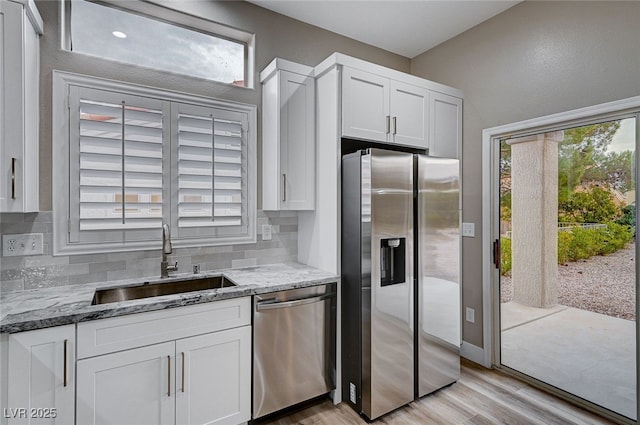 kitchen with sink, white cabinetry, backsplash, stainless steel appliances, and light stone countertops