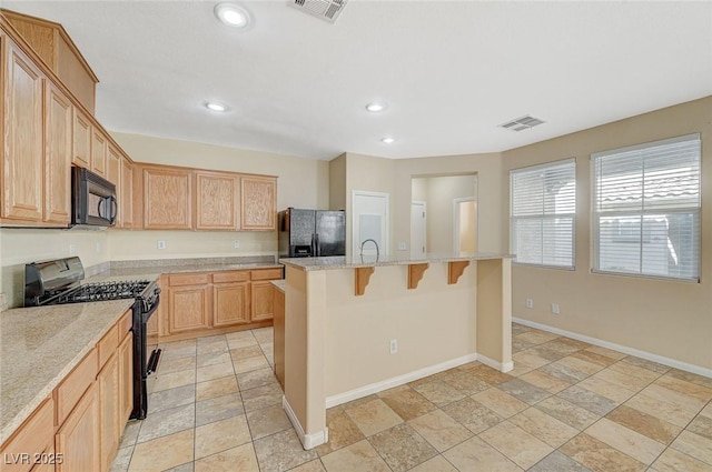 kitchen with a breakfast bar area, light stone counters, black appliances, a center island with sink, and light brown cabinetry