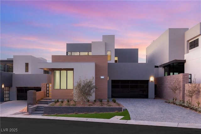 contemporary home with decorative driveway, an attached garage, and stucco siding