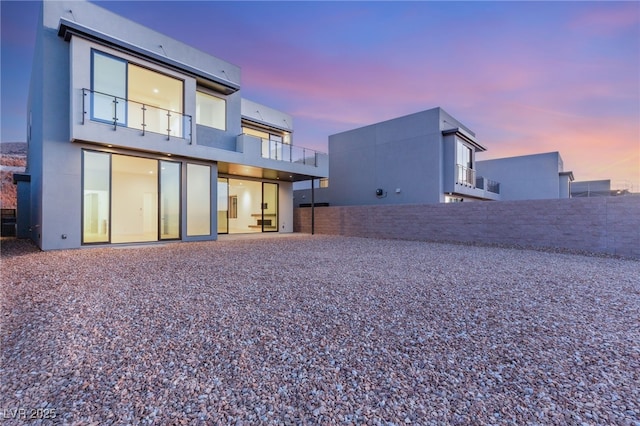 back of property at dusk featuring fence, a balcony, and stucco siding