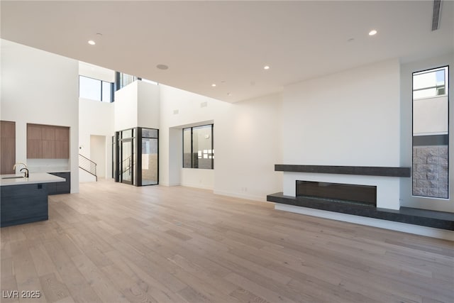 unfurnished living room featuring sink, light hardwood / wood-style flooring, and a high ceiling