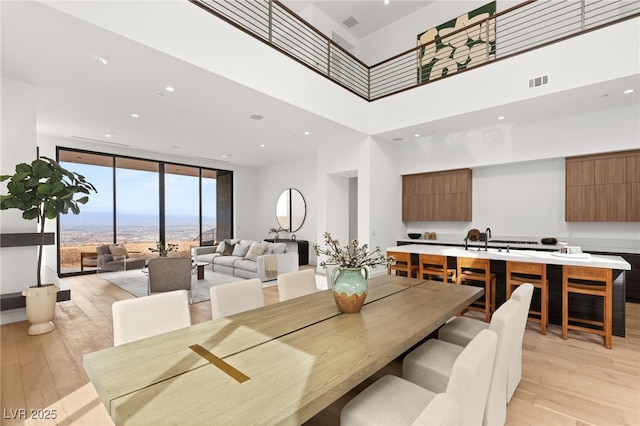 dining room featuring visible vents, a towering ceiling, light wood-style flooring, a wall of windows, and recessed lighting