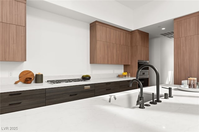 kitchen with visible vents, modern cabinets, light stone counters, stainless steel gas stovetop, and a sink