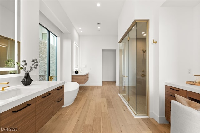 full bathroom featuring recessed lighting, two vanities, a stall shower, wood finished floors, and baseboards