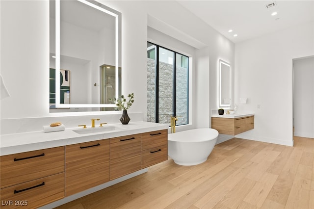 bathroom featuring wood finished floors, two vanities, a sink, visible vents, and a soaking tub