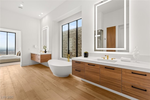 bathroom with wood finished floors, a sink, a freestanding tub, two vanities, and recessed lighting