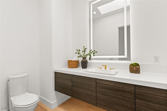 bathroom with a skylight, toilet, vanity, wood finished floors, and baseboards