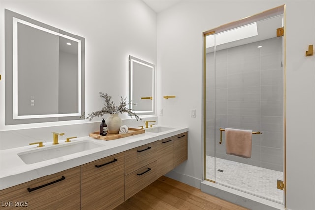 full bathroom with double vanity, a stall shower, a sink, and wood finished floors