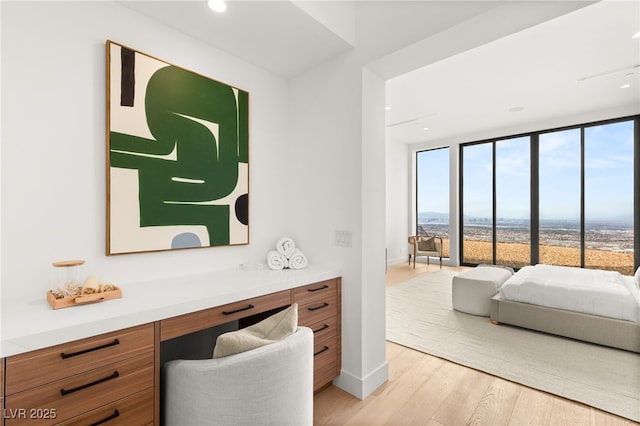 bedroom with baseboards, a wall of windows, light wood-style floors, built in desk, and recessed lighting