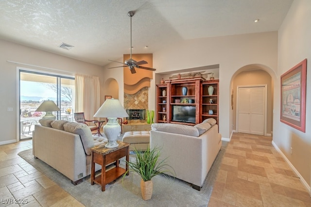 living room with a tiled fireplace, vaulted ceiling, ceiling fan, and a textured ceiling