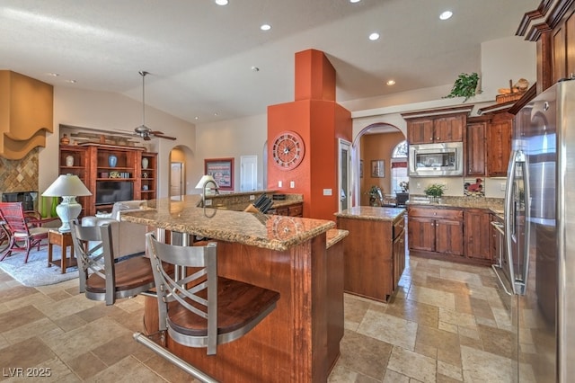 kitchen featuring lofted ceiling, light stone counters, pendant lighting, stainless steel appliances, and a kitchen island with sink