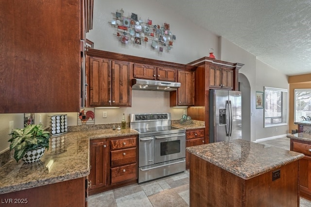 kitchen with stone counters, a kitchen island, a textured ceiling, and appliances with stainless steel finishes