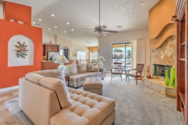 living room with a tiled fireplace, ceiling fan, and a textured ceiling