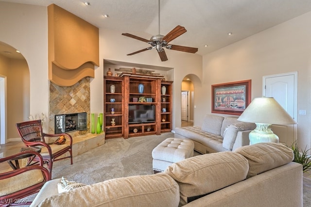 living room with a tile fireplace, carpet flooring, ceiling fan, and a towering ceiling