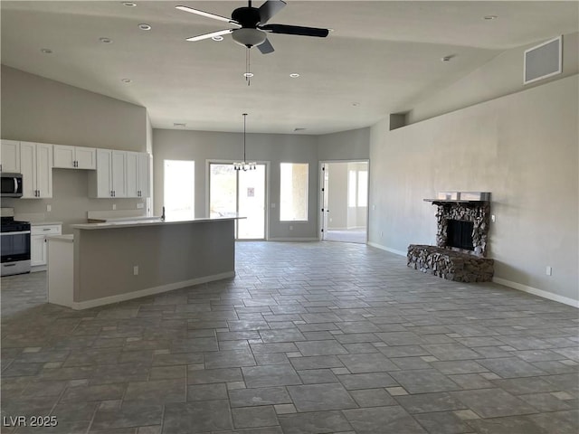 kitchen with ceiling fan with notable chandelier, a fireplace, white cabinetry, a high ceiling, and stainless steel appliances