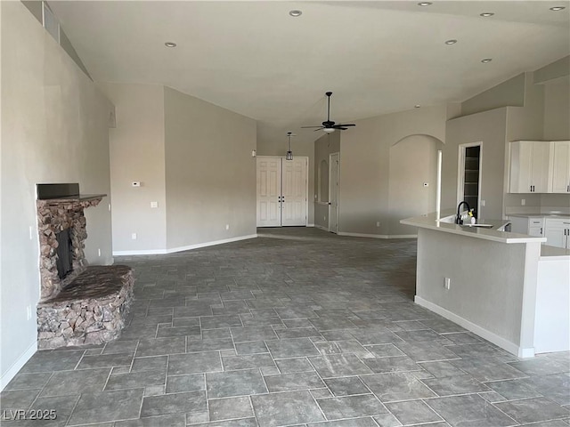 unfurnished living room with ceiling fan, a fireplace, sink, and a towering ceiling