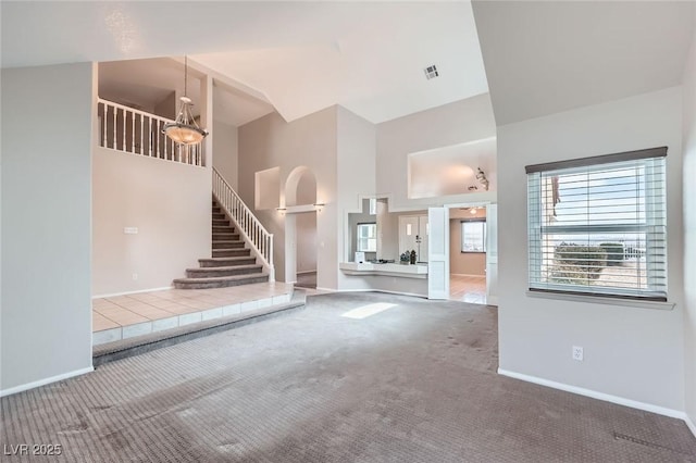 unfurnished living room featuring carpet, visible vents, baseboards, a high ceiling, and stairs